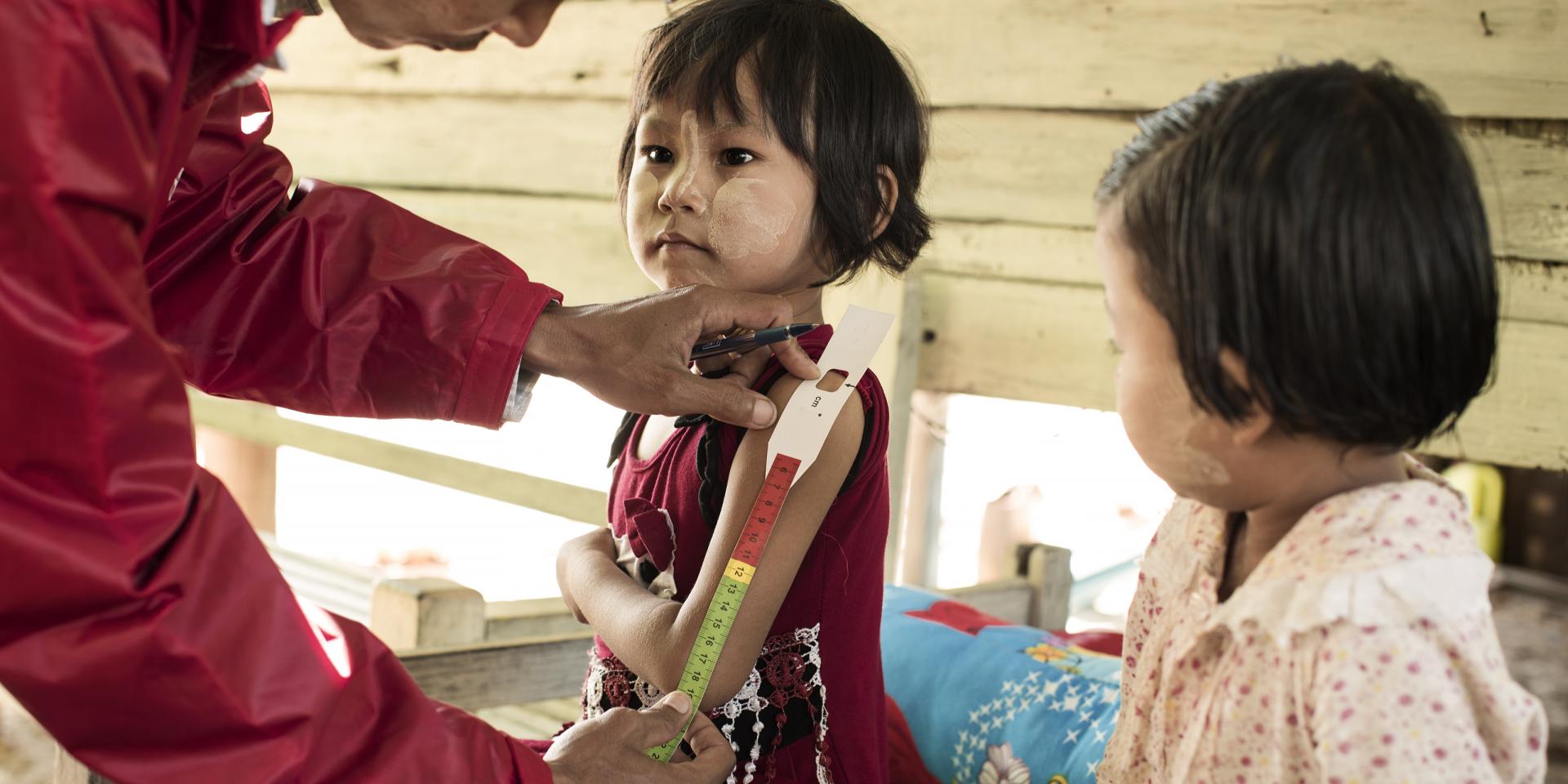 Myanmar. Un operatore sanitario di comunità misura la circonferenza del braccio di Mi Mi May, 5 anni. Un’altra bambina, al suo fianco, aspetta il suo turno per essere visitata.