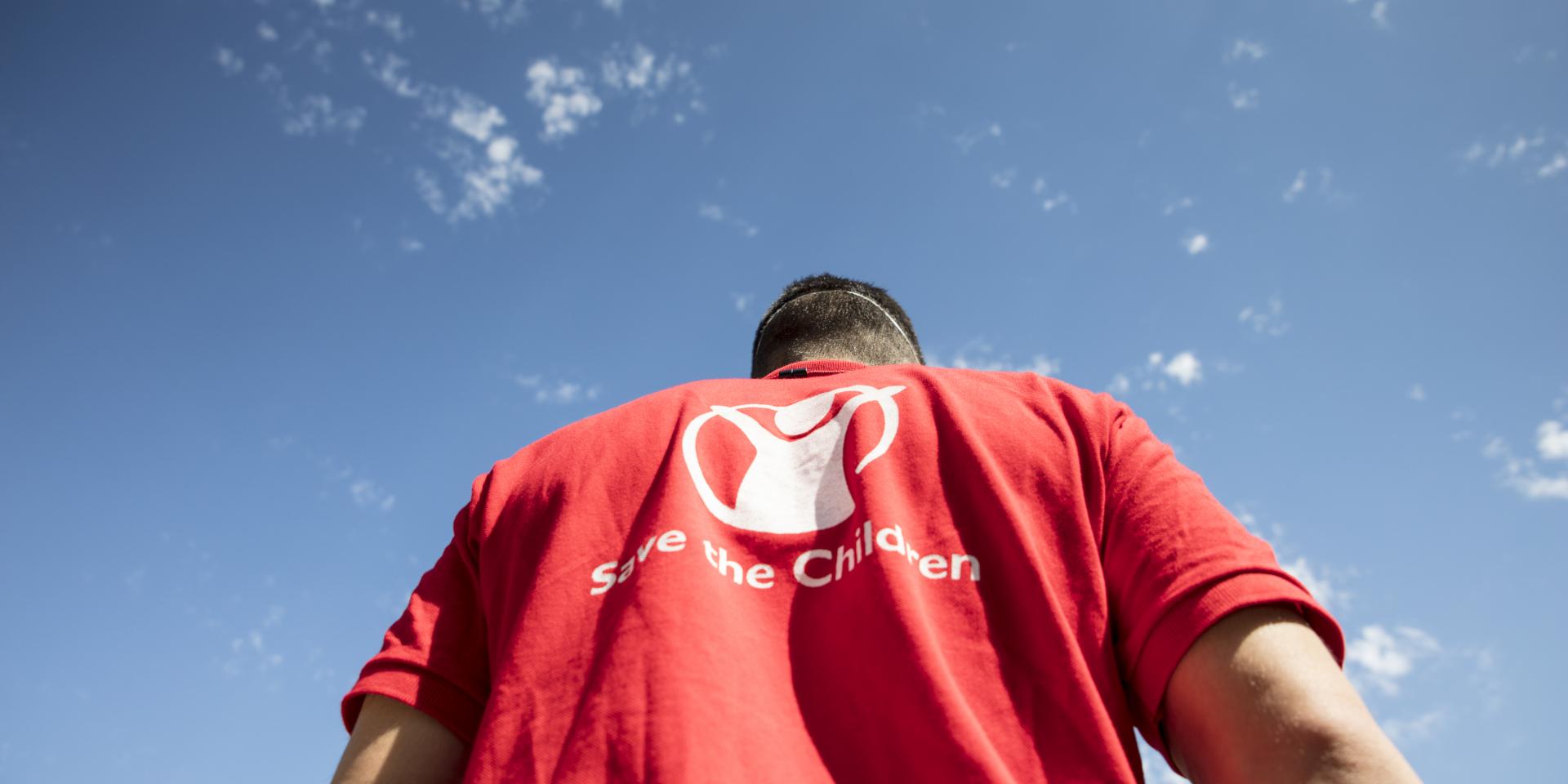 Un operatore indossa una maglietta rossa con il logo di Save the Children, che mette al centro la figura stilizzata di un bambino