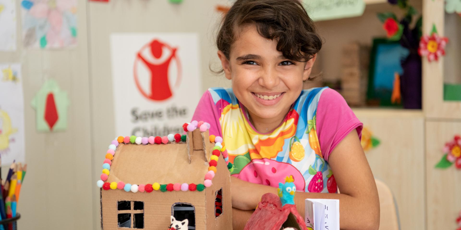 Naima, 12 anni, mostra fiera il suo lavoretto (una casetta di cartone) realizzato in un centro educativo di Save the Children in un campo rifugiati  siriani nel nord dell'Iraq.