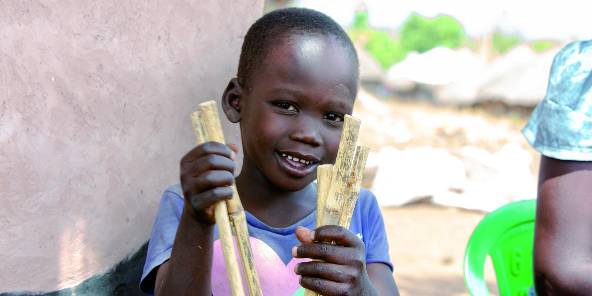 Un bambino ugandese tiene in mano dei bastoncini che usa per imparare a contare