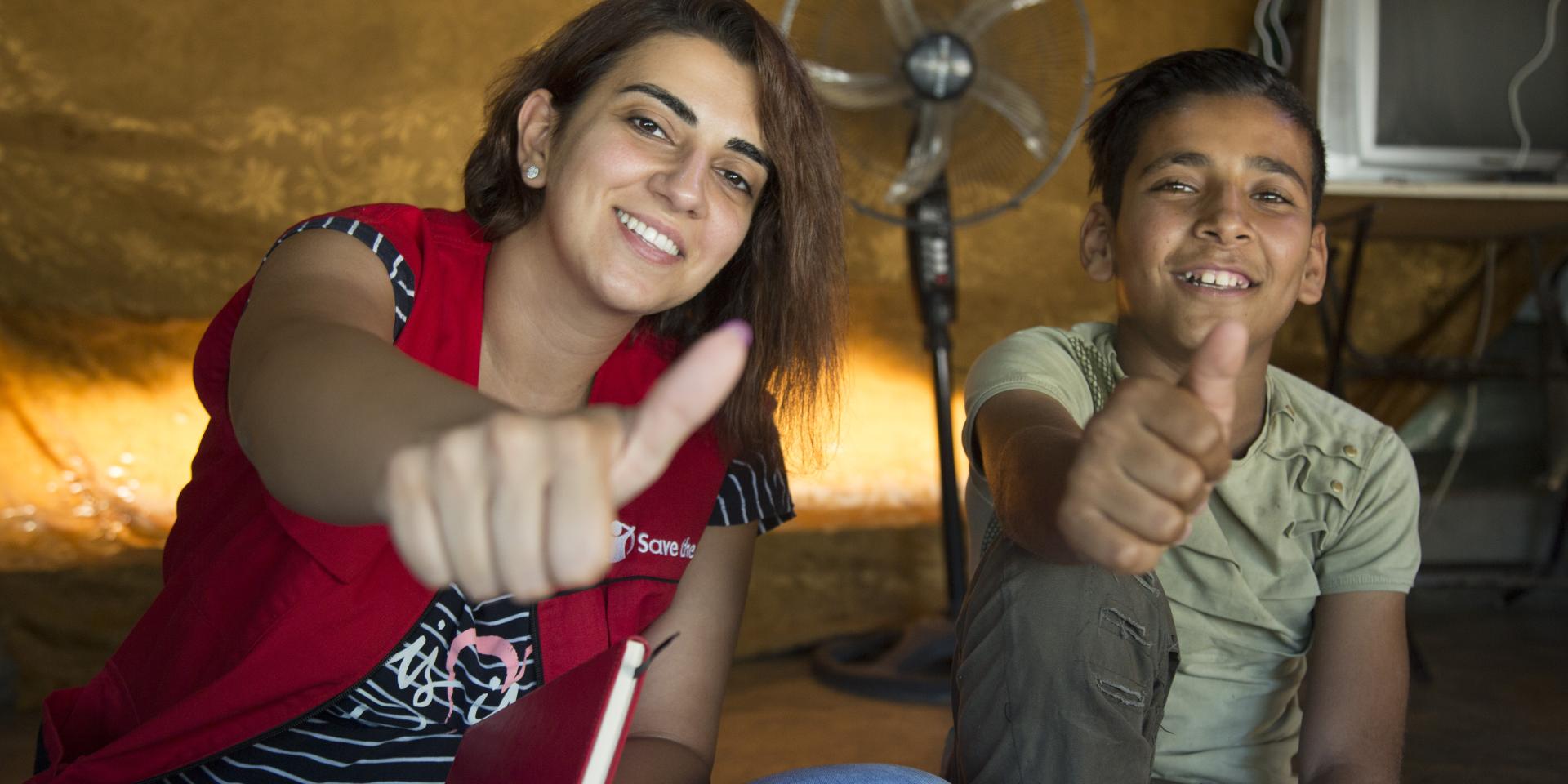 Un'operatrice e un bambino sorridono guardando l'obiettivo all'interno di una tenda in un insediamento informale nella Valle della Bekka, in Libano