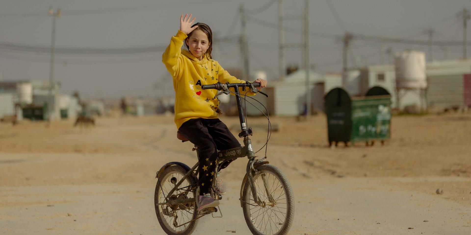 Una bambina di 13 anni pedala in bicicletta lungo una strada sterrata all'interno del campo rifugiati di Za'atari in Giordania