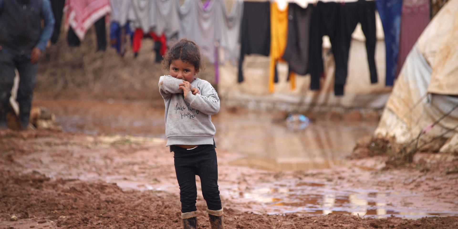 Una bambina davanti alla sua tenda, con i piedi immersi nel fango a causa di un alluvione, in un campo sfollati a Idlib, in Siria