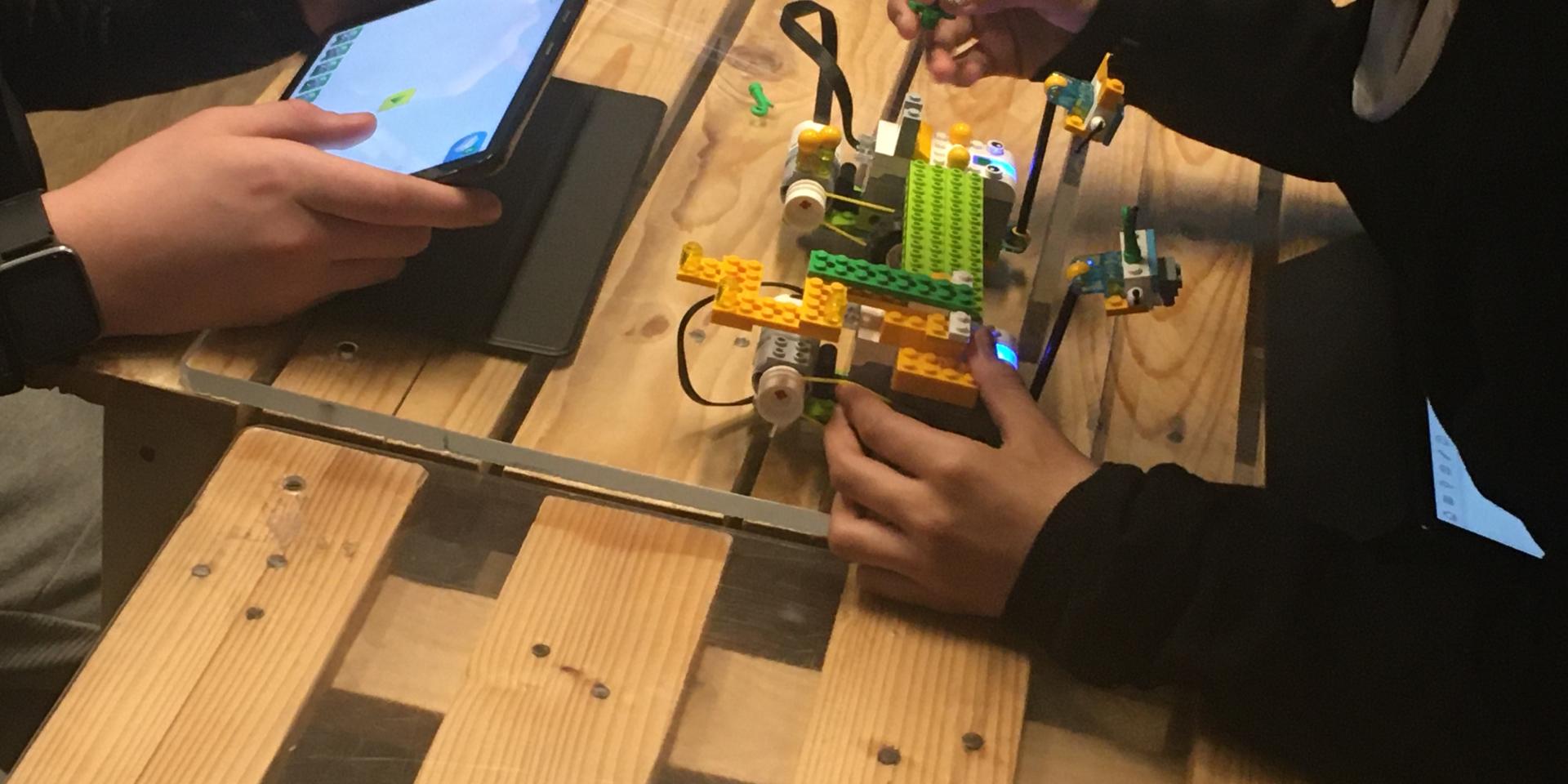 mani di due bambini che programmano e costruiscono un robot su un tavolo da lavoro.