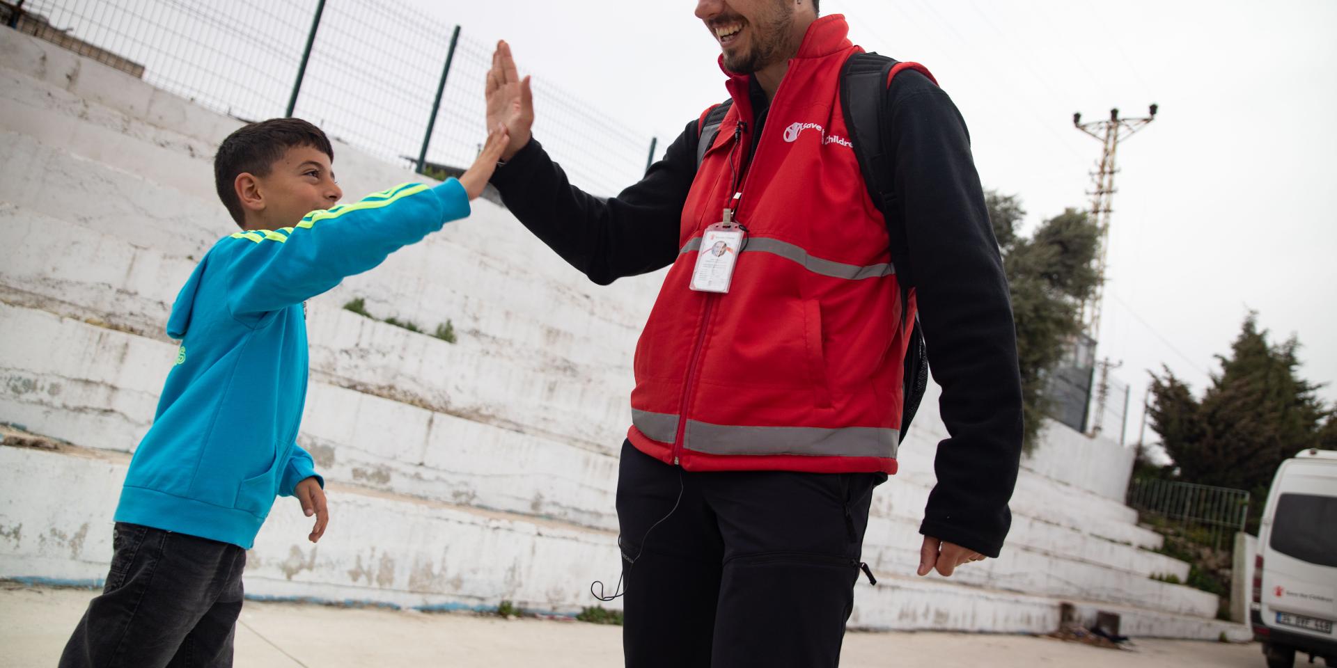 Un operatore con la pettorina rossa di Save the Children batte affettuosamente la mano a un bambino durante le attività di intervento psicosociale organizzate dall'Organizzazione per aiutare i bambini colpiti dal terremoto in Turchia nel 2023.