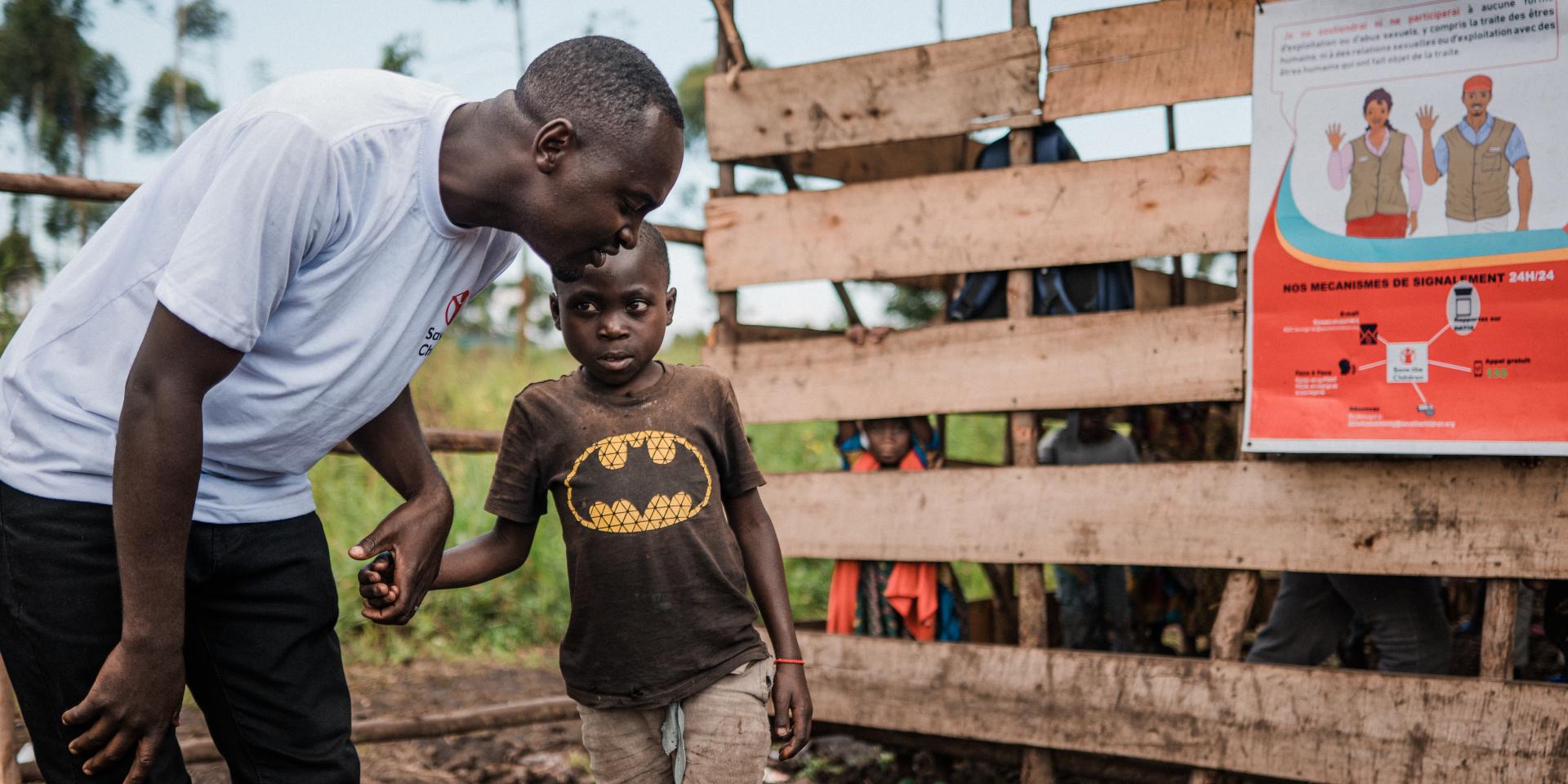 Un operatore si china sorridente per ascoltare un bambino, a cui dà la mano, nell'area all'aperto di uno Spazio a Misura di Bambino per rifugiati della Repubblica Democratica del Congo.