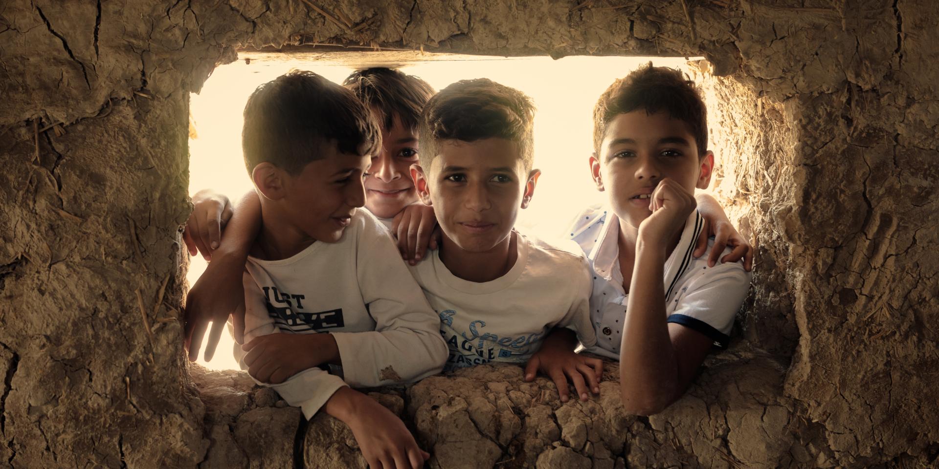 Quattro bambini si affacciano da una finestra di un muretto fatto di terra, in un villaggio in Iraq