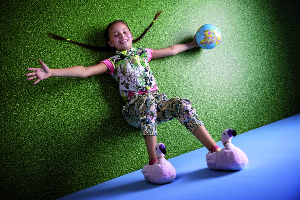 Una bambina sorridente sdraiata per terra con un mappamondo in mano