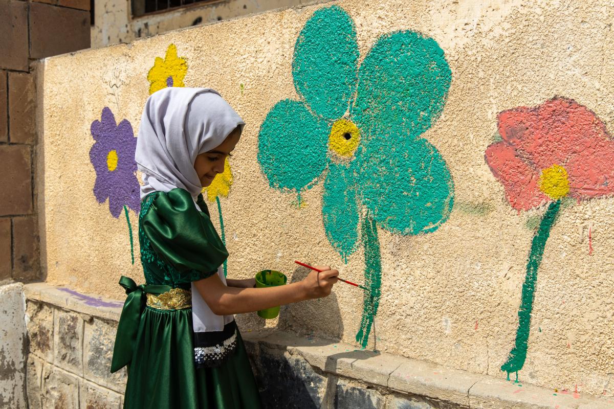 Una bambina yemenita dipinge fiori, simbolo di rinascita, sul muro di una scuola distrutta dalle bombe