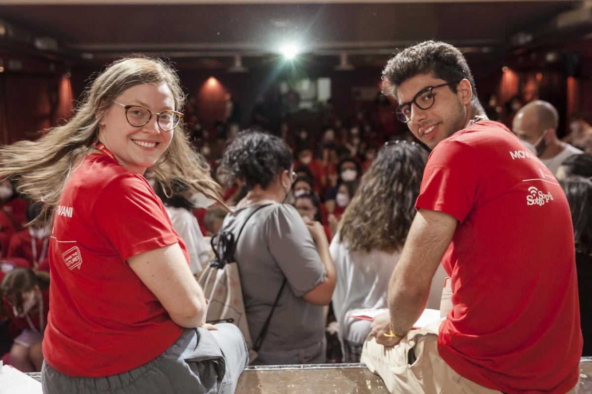 Durante la plenaria di inaugurazione del festival, due volontari, seduti di spalle all'obiettivo, si voltano sorridenti verso la fotocamera