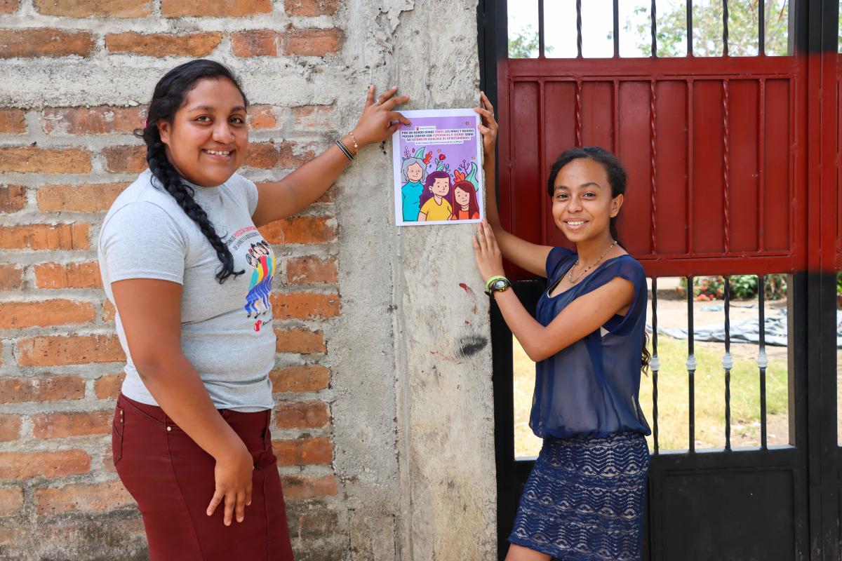 Due ragazze sorridenti mostrano una locandina di una iniziativa di Save the Children
