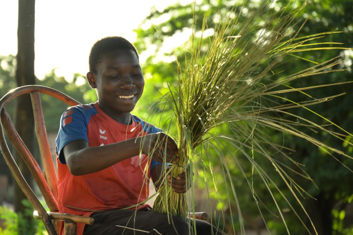 Tiago, 16 anni, mentre costruisce una scopa con l'erba per aiutare la sua comunità, Malawi