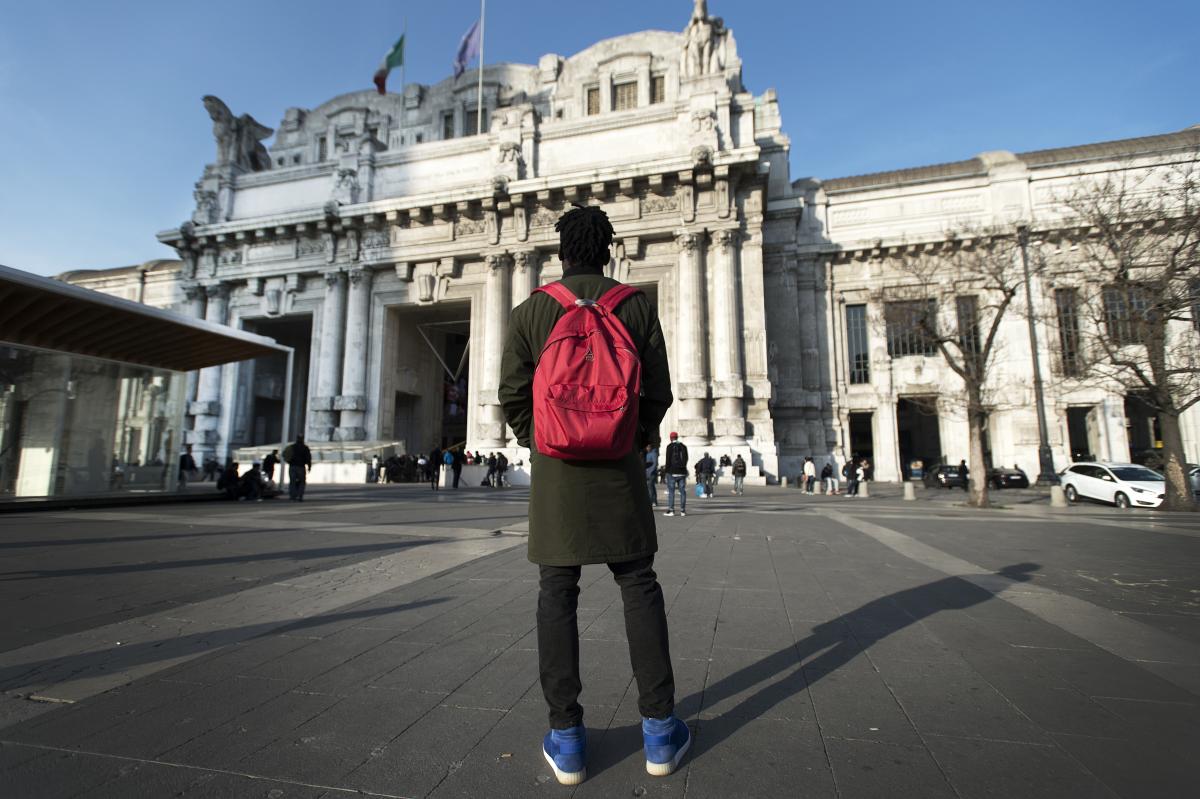 Un ragazzo con uno zaino rosso sulle spalle guarda verso la stazione centrale di Milano