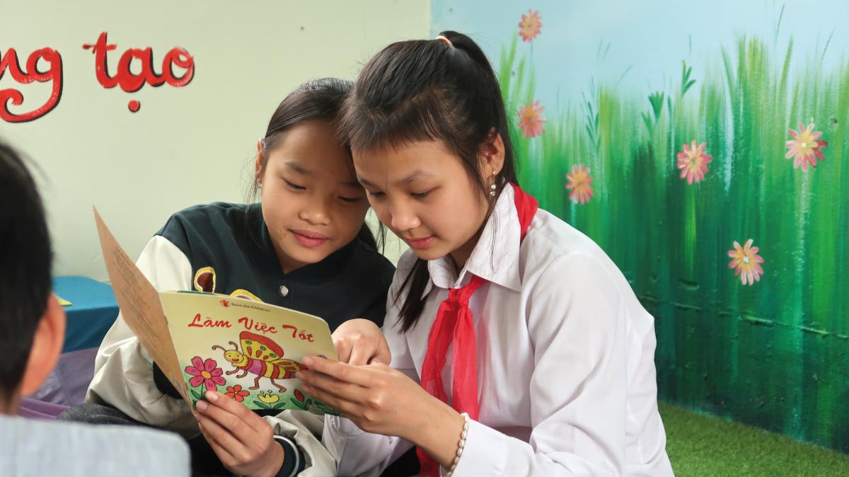 Due bambine di 10 anni leggono un libro dal titolo “Fai buone azioni” nella biblioteca della loro scuola in Vietnam.