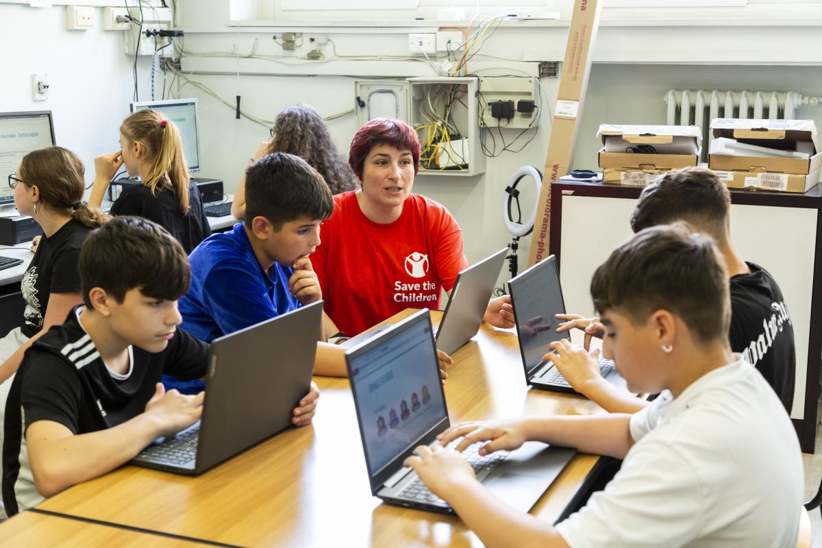 Una operatrice guida quattro ragazzi nel fare esperienza al computer all'interno di una scuola che fa parte del progetto Connessioni Digitali