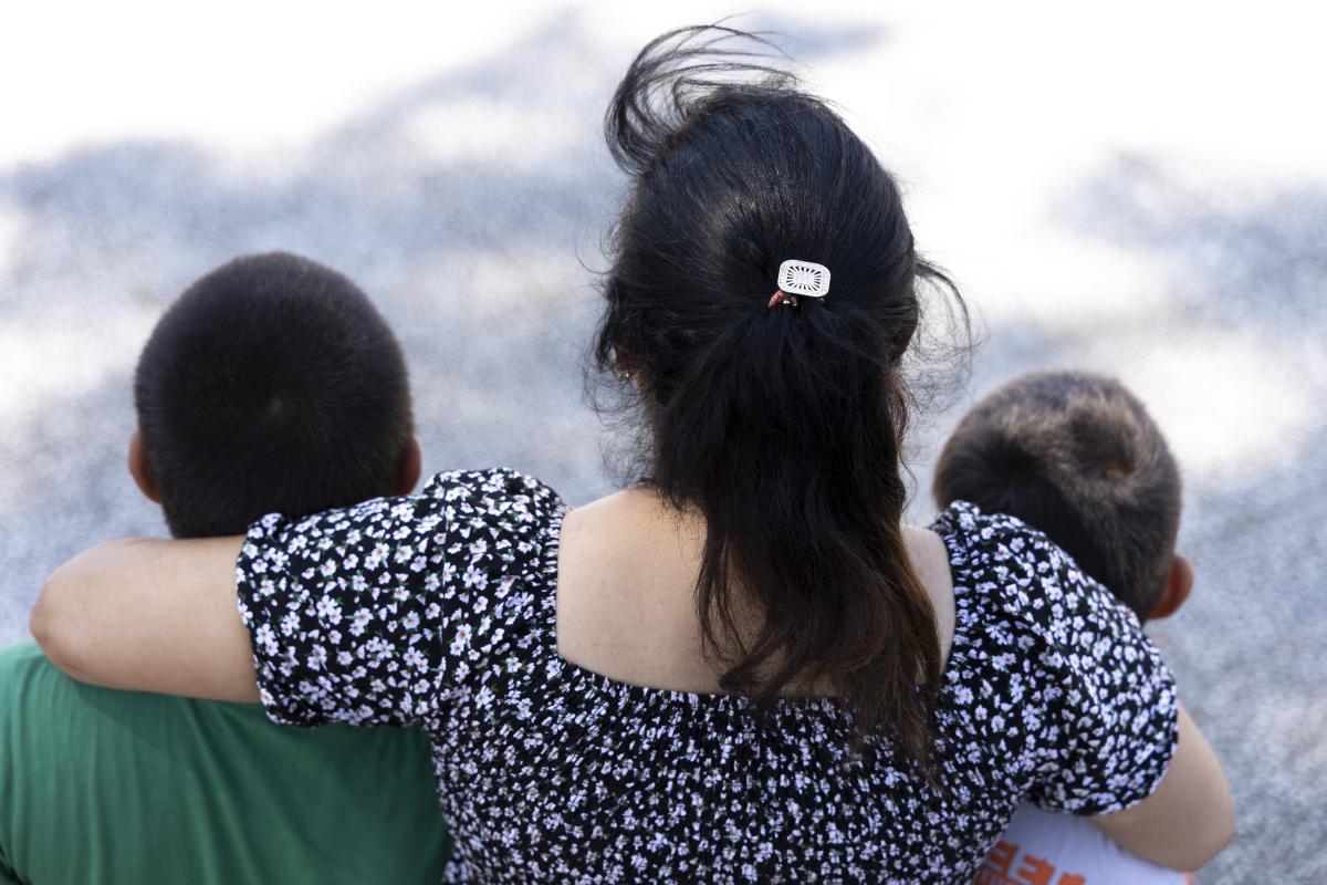 Una donna abbraccia due bambini, ritratti tutti di spalle