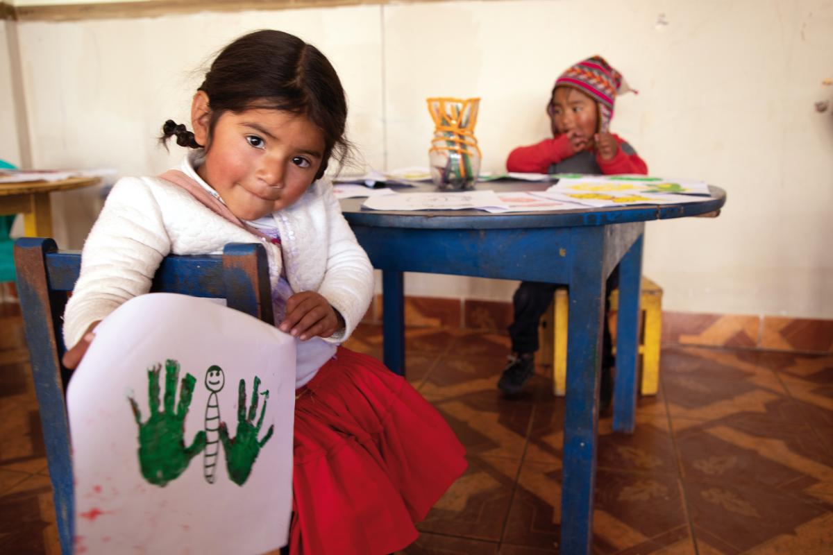 Una bambina boliviana di tre anni mostra la farfalla che ha disegnato su un foglio. Le ali delle farfalle sono fatte con l’impronta delle mani della bambina.