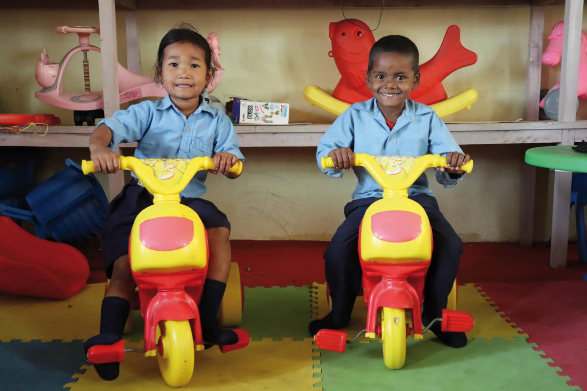 una bambina di 6 anni e un bambino di 5 anni giocano su due tricicli in un centro di educazione prescolare in Nepal.