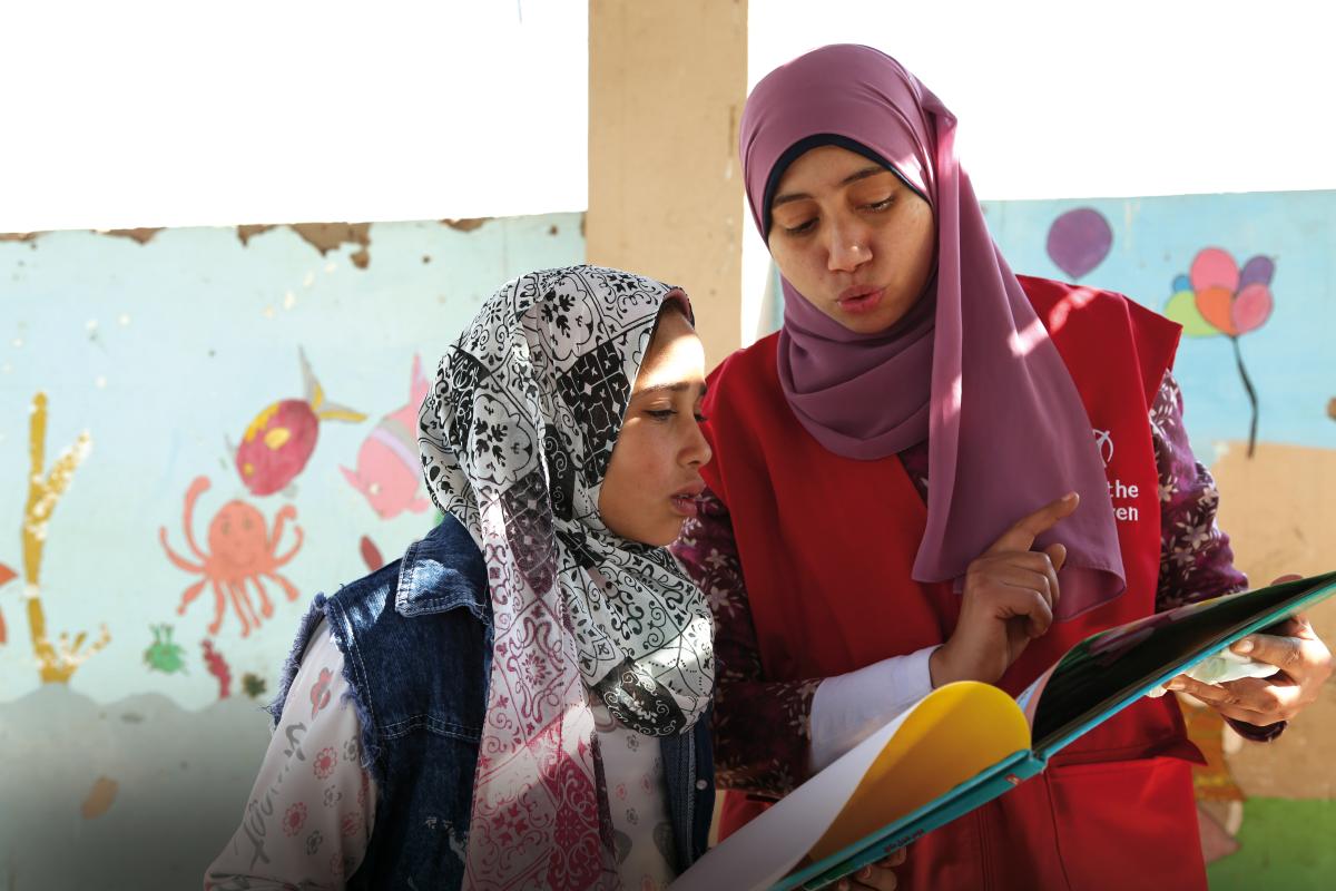 Una bambina di 12 anni legge una storia con l’aiuto di un’operatrice Save the Children, in Egitto.